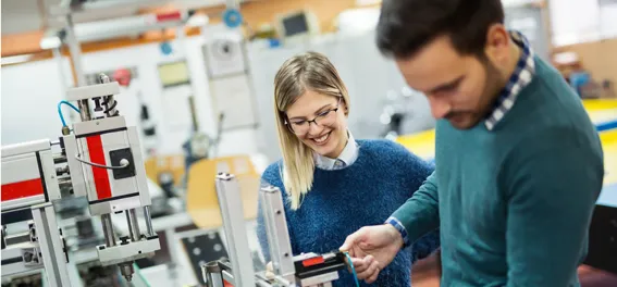 Frau und Mann arbeiten gemeinsam an einer Maschine in einer industriellen Fertigungsumgebung.
