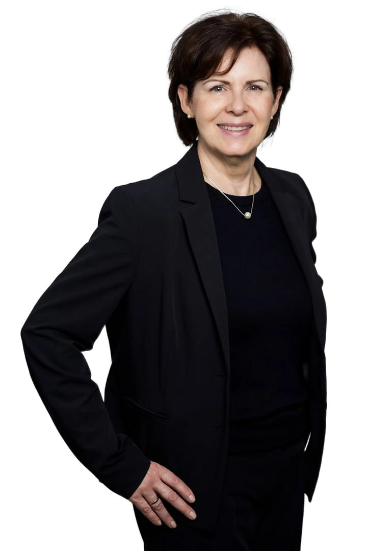 Porträt von Katja Hoffmeister vor weißem Hintergrund. Sie trägt einen schwarzen Blazer über einem schwarzen Oberteil und blickt lächelnd in die Kamera.