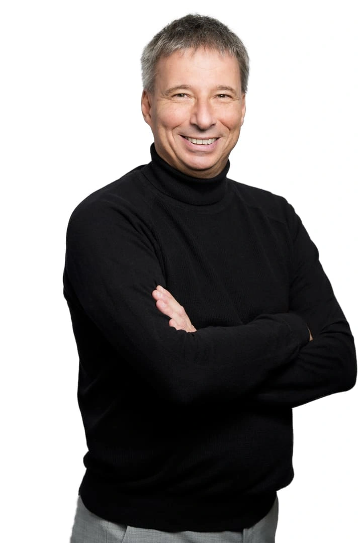 Porträt von Stefan Pollpeter vor weißem Hintergrund. Er trägt einen schwarzen Rollkragenpullover, hat die Arme verschränkt und blickt mit einem freundlichen Lächeln direkt in die Kamera.